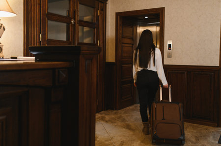 Woman arrives at elegant hotel lobby, pulling suitcase and waiting for elevator before checking in on a business or leisure tripの写真素材