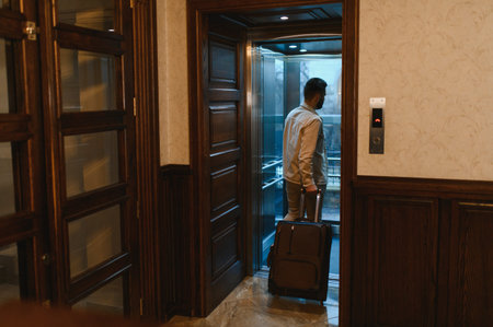 Man entering a modern glass elevator with his luggage, preparing to travel or checking out from a hotelの写真素材