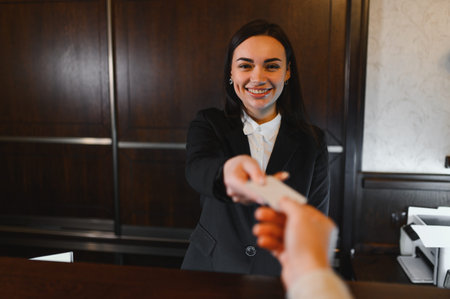 Friendly hotel receptionist providing excellent service, handing a key card to a guest at the front deskの写真素材