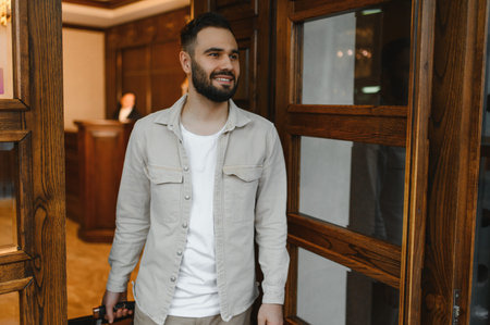Young happy man with suitcase smiling, walking into a luxury hotel lobby, arriving for vacation travelの写真素材