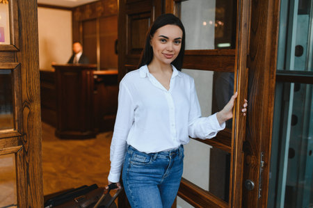 Young woman traveler entering hotel lobby with luggage, smiling and ready to check in for business trip or vacationの写真素材