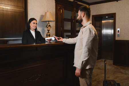 Guest making a payment with a smartphone at the reception desk in a hotel lobby, using a contactless pos terminalの写真素材