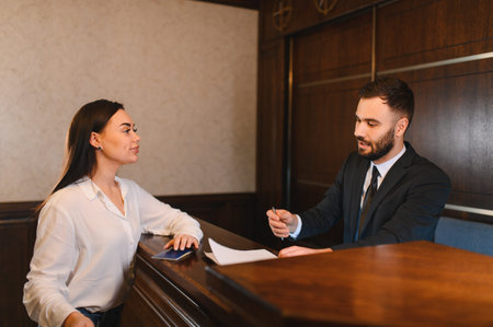 Guest standing at hotel reception desk, talking to male receptionist about current booking information and check in detailsの写真素材
