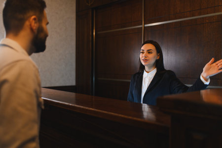 Hotel employee providing professional hospitality service, assisting a male guest at the reception desk in a lobbyの写真素材