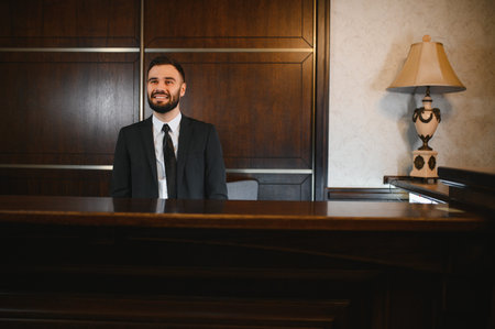 Young man working as a concierge, offering welcoming service in a hotel lobby. Symbolizing hospitality and assistanceの写真素材