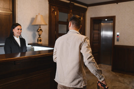 Man with luggage approaching smiling receptionist at front desk for check in. Hotel guest arriving at luxurious accommodationの写真素材