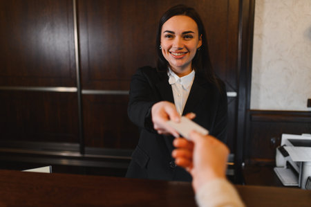 Smiling hotel receptionist hands a key card to a guest at the front desk, professional welcome and check in service in lobbyの写真素材