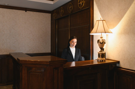 Young woman working at a hotel reception desk, providing professional hospitality service in a traditional, elegant lobby interiorの写真素材