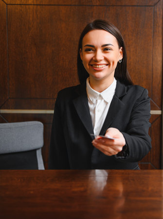 Smiling hotel receptionist working at a lobby desk, handing over a key card to a guest, offering friendly serviceの写真素材