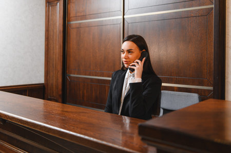 Female professional working at hotel front desk, providing service and communicating with guests using a corded landline phoneの写真素材