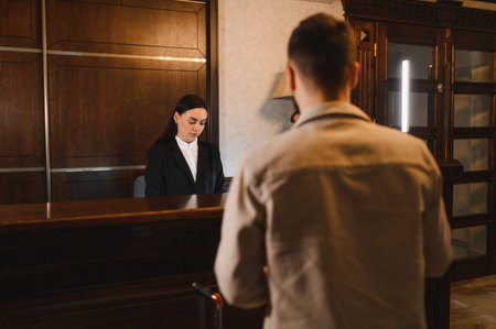 Guest interacting with a female receptionist behind the wooden counter in a hotel lobby, completing check in proceduresの写真素材