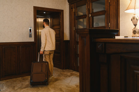 Man entering hotel elevator with suitcase in modern lobby, guest arriving or departing during business trip or vacation stayの写真素材