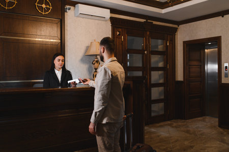 Man completing hotel check in process, receiving a key card from a friendly female receptionist at the lobby counterの写真素材