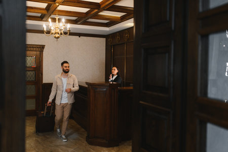 Man entering a hotel lobby with a suitcase, approaching the reception desk, traveling for business or leisureの写真素材