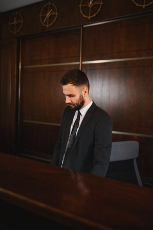Hotel receptionist wearing a suit and looking down, providing professional service in a modern lobby interior with time zone clocksの写真素材