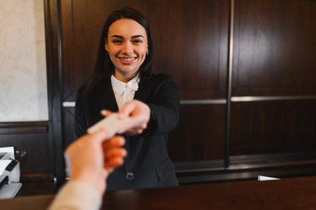 Friendly hotel receptionist at the front desk handing a key card to a guest, providing excellent customer serviceの写真素材