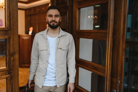 Young man with a beard entering a luxury hotel lobby, carrying luggage, preparing for check in at reception deskの写真素材
