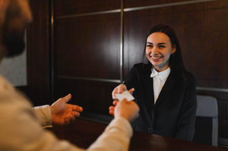 Hotel receptionist smiling, handing a key card to a guest at the reception desk, providing efficient check in serviceの写真素材