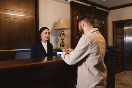 Hotel receptionist greeting a guest at the front desk in a luxurious hotel lobby, providing professional service for accommodationの写真素材