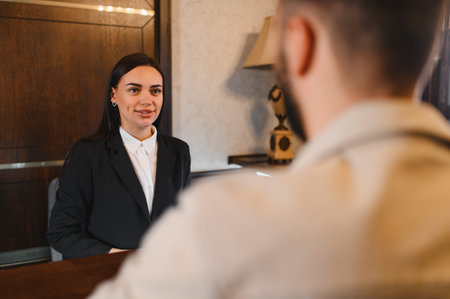 Smiling woman working as a hotel receptionist, attending to a guest at the reception desk in a contemporary lobbyの写真素材
