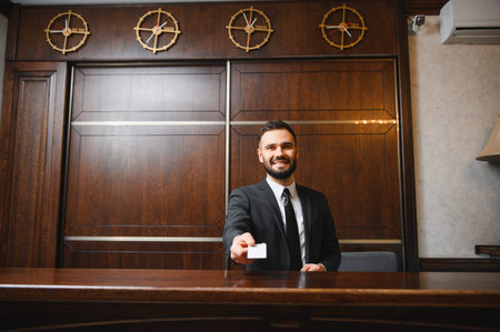 Smiling man providing friendly service at hotel reception, handing over a room key or access card. Hospitality conceptの写真素材