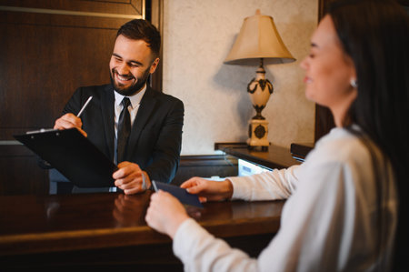 Male hotel receptionist smiling and helping a female guest with check in paperwork at the front desk, providing excellent serviceの写真素材