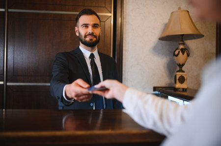 Hotel employee extending a room key card to a guest at the reception desk, focusing on hospitality and serviceの写真素材