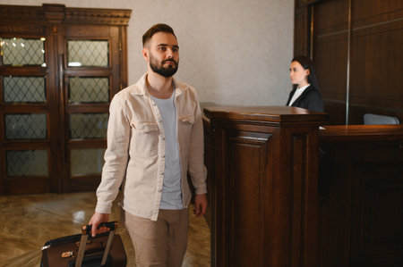 Man with a suitcase checking in at hotel reception desk. Female receptionist assisting guests in a welcoming lobby areaの写真素材