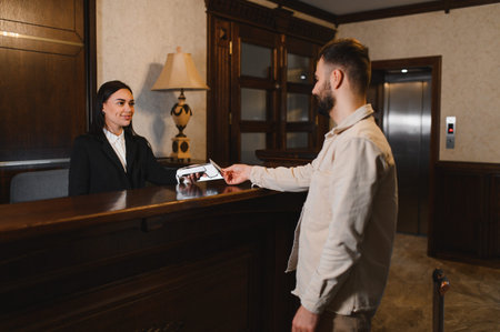 Guest completing payment with a credit card at the lobby reception, interacting with a smiling hotel receptionistの写真素材