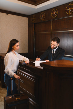 Female traveler arriving, receiving room key card from male receptionist at luxurious hotel lobby, completing check in processの写真素材