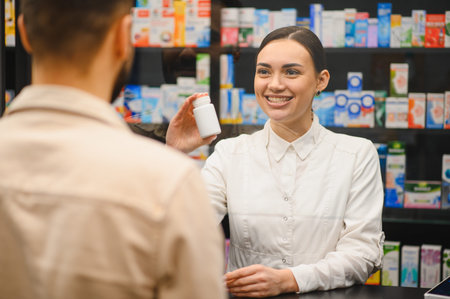 Smiling female pharmacist holding medicine bottle, discussing healthcare information and prescription with a male customerの写真素材
