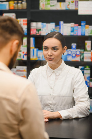 Pharmacist standing at counter, interacting with a customer and providing healthcare advice in a modern pharmacyの写真素材