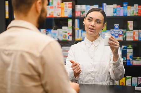 Pharmacist holding a medication bottle, talking with a customer at the pharmacy counter, offering professional adviceの写真素材