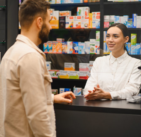 Pharmacist standing at counter talking to male client, providing consultation and customer service in a retail pharmacyの写真素材