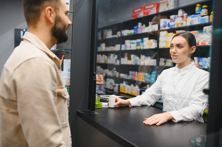 Pharmacist standing at a counter, handing medication to a male customer, ensuring safe and professional healthcare serviceの写真素材