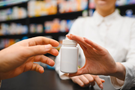 Pharmacist's hands giving a white unbranded medicine bottle to a customer in a pharmacy, symbolizing health careの写真素材