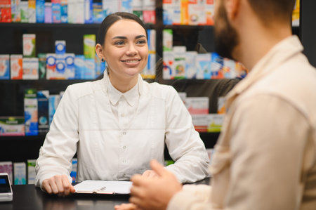 Woman pharmacist smiling, assisting client with medication information, offering healthcare advice at a pharmacy counterの写真素材