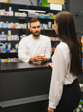 Male pharmacist working at pharmacy counter, consulting a female customer about prescription medicine and healthcareの写真素材