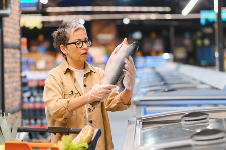 Customer carefully examining raw fish, wearing gloves, making a healthy food choice in the grocery storeの写真素材