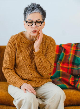 Woman experiencing intense dental pain, grimacing and holding her cheek, reflecting discomfort and oral health issuesの写真素材