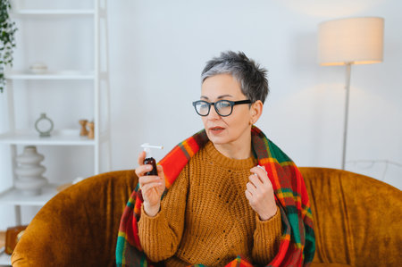 Woman feeling unwell using a throat spray for cold or flu symptoms, wrapped in a warm blanket...