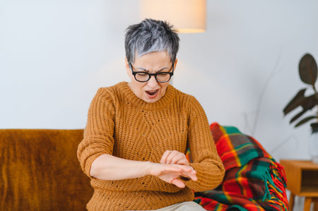 Senior woman suffering from skin irritation, examining her wrist with an expression of discomfort. Itching and dermatitis on skinの写真素材