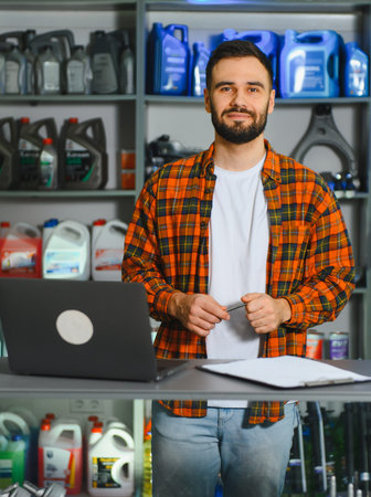 Service advisor smiling while standing at a desk with a laptop and clipboard, stock of engine fluids in the backgroundの写真素材