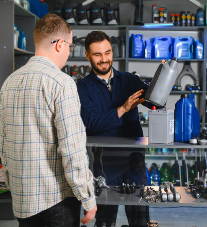 Mechanic assisting a client with product selection, holding motor oil bottle and showing car parts in an automotive storeの写真素材