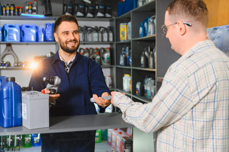 Auto service mechanic holding an impact wrench and discussing car parts with a male customer about...