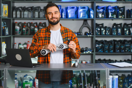 Happy bearded salesman standing in auto parts store, holding a car suspension arm, looking at cameraの写真素材
