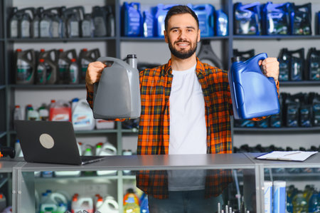 Smiling man working in an auto parts store, presenting two bottles of motor oil, standing behind a counter with a laptopの写真素材