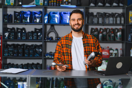 Young male seller standing behind the counter in an auto parts store, holding car spares. Auto service conceptの写真素材