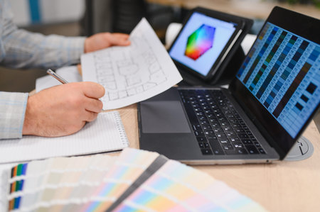 Person designing interior spaces, holding a blueprint, writing notes, and using digital color...