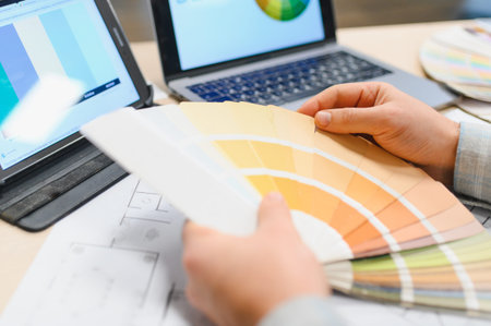 Creative professional hands using color palette swatches with digital tablet, laptop, and blueprint for interior design projectの写真素材